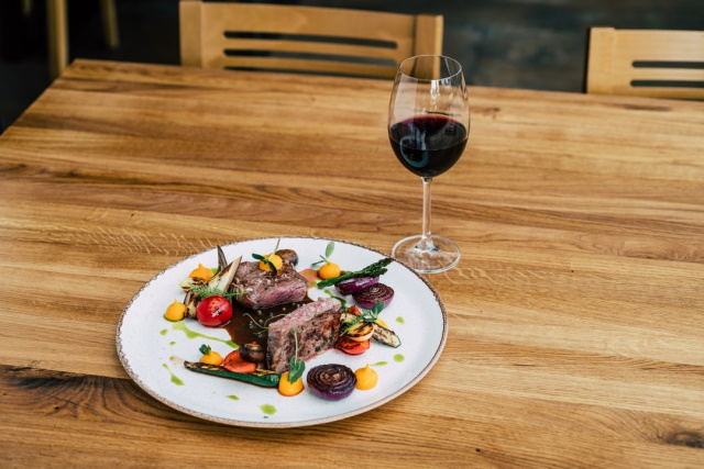 Artfully plated seared steak on a plate with roasted vegetables and glass of red wine